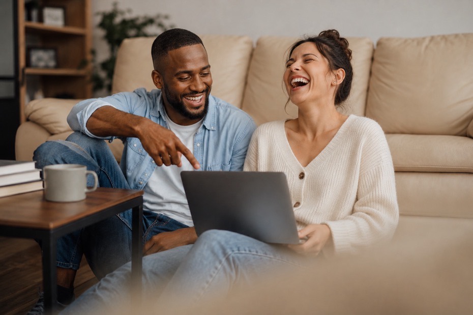 Couple smiling while looking at a laptop in their living room