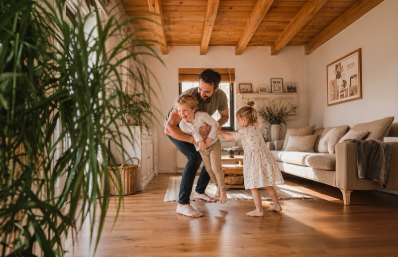 Parent dancing with two young children in a bright living room